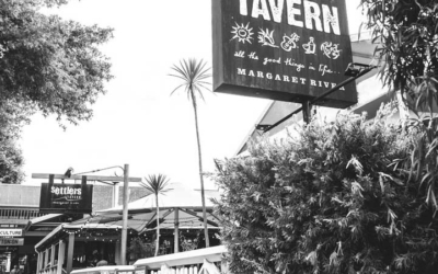 Settlers_Tavern_Food_OBJ886844 Black and white photo of Settlers Tavern entrance with prominent sign, trees, and a wooden fence lining the path.
