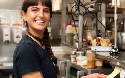 Settlers_Tavern_Food_OBJ886903 A woman with braided hair stands in a commercial kitchen, smiling while holding a receipt.