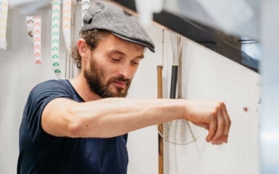 Settlers_Tavern_Food_OBJ886941 A man wearing a cap sprinkles seasoning while cooking in a kitchen.