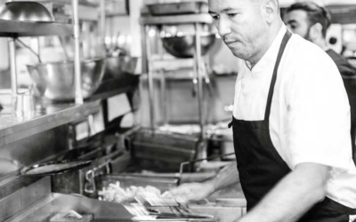 Settlers_Tavern_Food_OBJ887092 A chef in a kitchen wearing an apron cooks food on a stovetop, surrounded by cooking equipment.