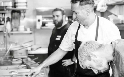 Settlers_Tavern_Food_OBJ887102 Chefs in a busy kitchen, one man cooking at the stove while others observe and assist, surrounded by various cooking utensils and equipment.