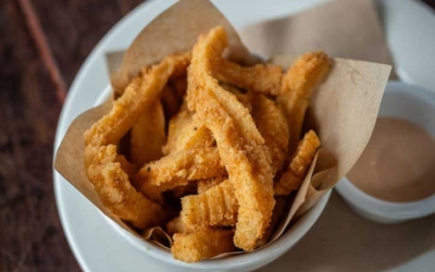 Settlers_Tavern_Food_OBJ887146 A cup of fried churros is served with dipping sauce on a wooden table.