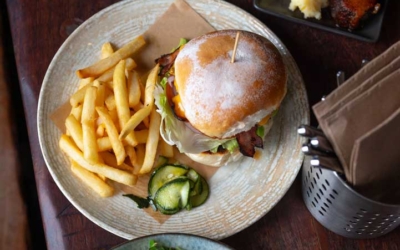 Settlers_Tavern_Food_OBJ887162 A table with a chicken parmigiana, a burger with fries, a plate of sticky ribs with mashed potatoes, and a salad with red chili peppers and greens.