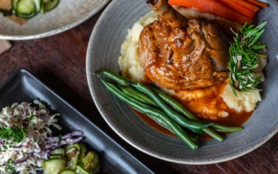 Settlers_Tavern_Food_OBJ887175 A table with a burger and fries, roasted chicken with mashed potatoes, carrots, and green beans, and a dish of grilled meat with mashed potatoes and coleslaw.