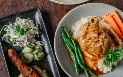 Settlers_Tavern_Food_OBJ887178 Three dishes on a wooden table: a burger with fries, roast chicken with mashed potatoes and vegetables, and beef brisket with coleslaw and mashed potatoes.