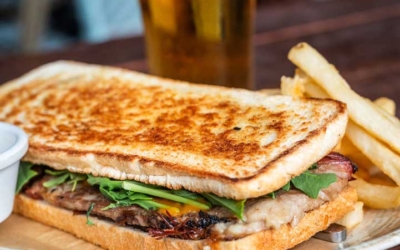 Settlers_Tavern_Food_OBJ887257 Toasted sandwich with greens and meat, served with fries and a glass of beer on a wooden table.