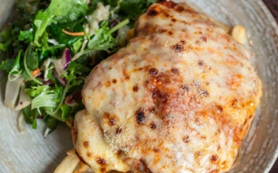 Settlers_Tavern_Food_OBJ887268 A plate with chicken parmigiana on top of fries, accompanied by a side salad. A glass of beer is in the background.