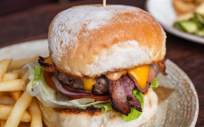 Settlers_Tavern_Food_OBJ887335 A cheeseburger with bacon, lettuce, and sauce is served on a plate with fries and pickles, garnished with a skewer.