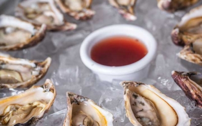 Settlers_Tavern_Food_OBJ887342 A plate of half-shell oysters arranged in a circle on ice with a small bowl of red sauce in the center.