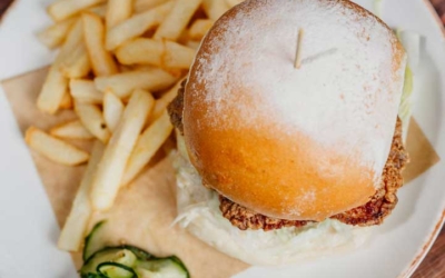 Settlers_Tavern_Food_OBJ887349 A plate with a burger, fries, and sliced cucumbers on a wooden table.