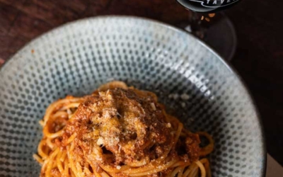 Settlers_Tavern_Food_OBJ887398 Spaghetti with meat sauce and grated cheese on a plate next to a glass of red wine on a wooden table.