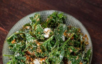 Settlers_Tavern_Food_OBJ887418 A plate of spinach salad with crumbled cheese and nuts on a wooden table.