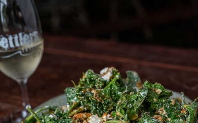 Settlers_Tavern_Food_OBJ887420 A plate of salad with greens and toppings next to a glass of white wine on a wooden table.