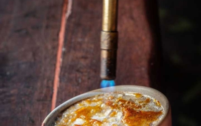 Settlers_Tavern_Food_OBJ887439 A culinary torch caramelizes sugar on a crème brûlée in a small dish on a wooden table.