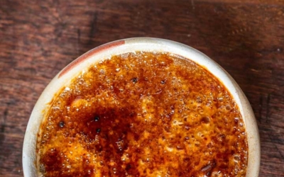 Settlers_Tavern_Food_OBJ887456 A bowl of crème brûlée with a caramelized, golden-brown sugar crust on a wooden surface.