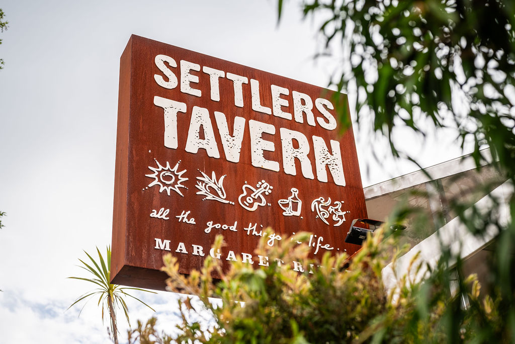 Settlers_Tavern_Food_OBJ887488 Sign for Settlers Tavern with icons and the phrase "all the good things in life," surrounded by trees. Located in Margaret River.