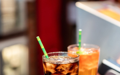 Settlers_Tavern_Food_OBJ887719 Two glasses on a wooden counter: one filled with a dark beverage and ice, the other with a lighter drink. Both glasses have green striped straws.